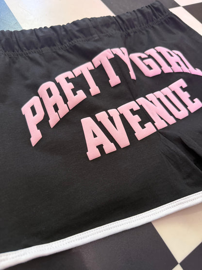 Black shorts with pink text 'PRETTY GIRL AVENUE' on a checkered floor.